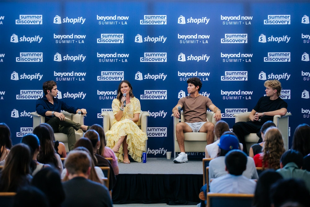 Four people seated on stage at Shopify Beyond Now Summit LA with an audience watching.