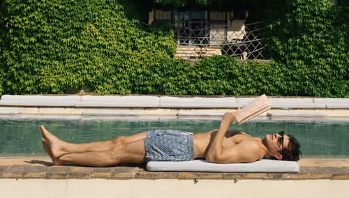 Peninsula Swim&Wear: man reading by a pool in swim shorts