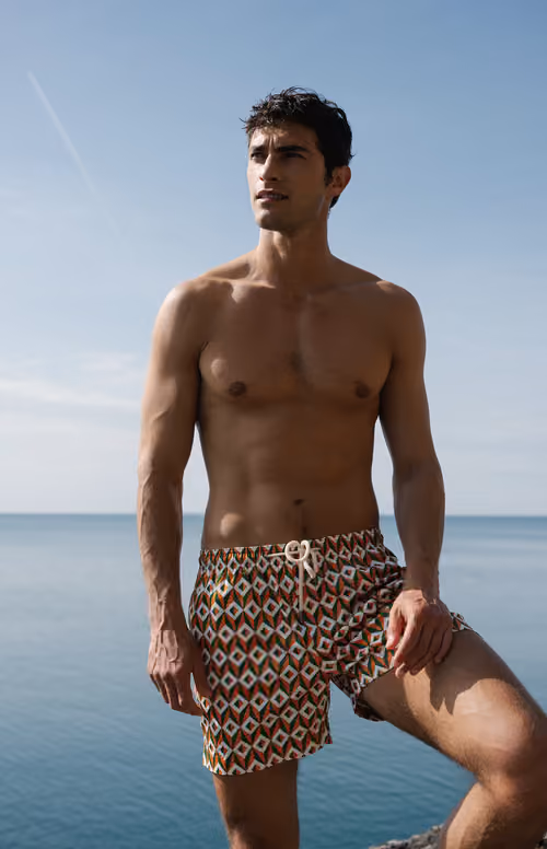 Peninsula Swim&Wear: model in patterned swim shorts by the sea