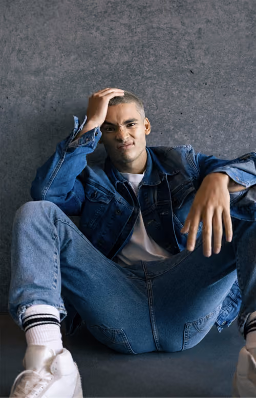 Gas Jeans: man in denim sitting against a concrete wall