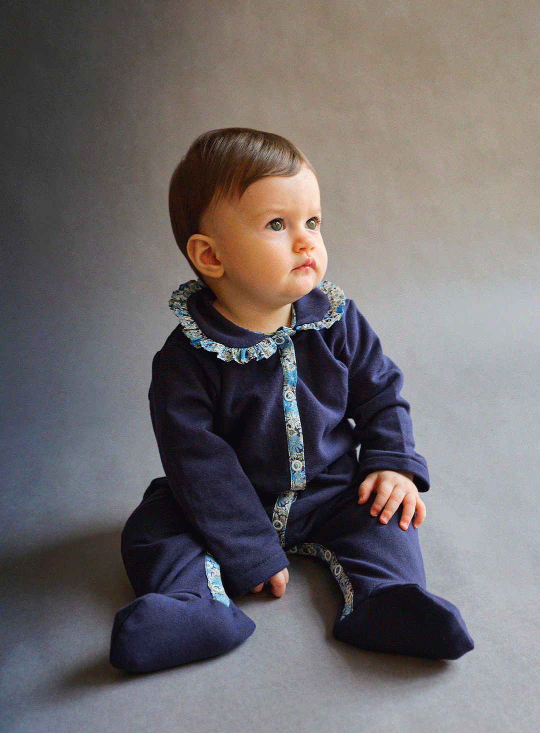 Baby in a navy sleepsuit with Liberty print trim