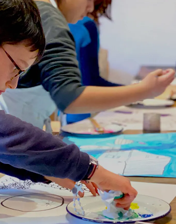 Enfant concentré utilisant une éponge pour peindre sur une feuille lors d'un atelier d'art.