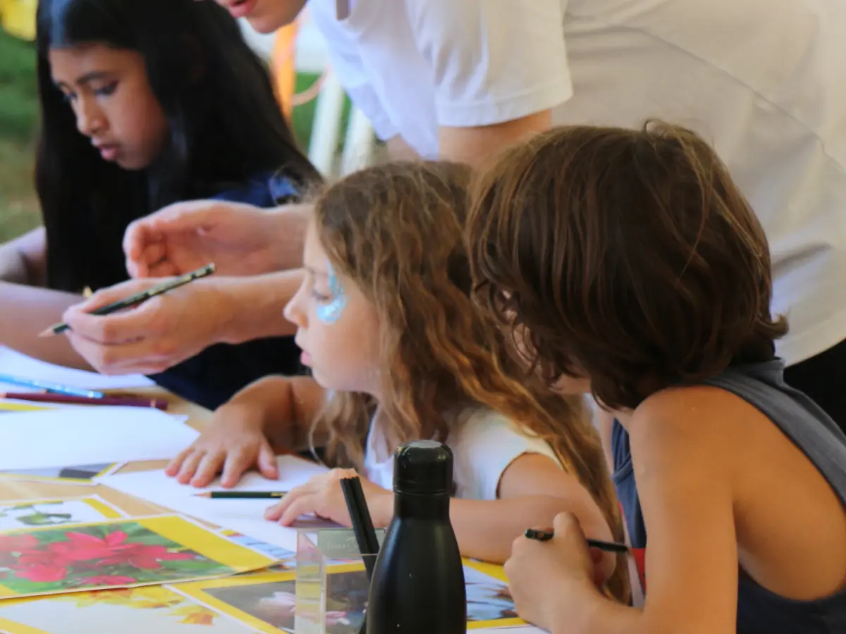 Enfants assis à une table en train de dessiner avec un adulte les guidant.