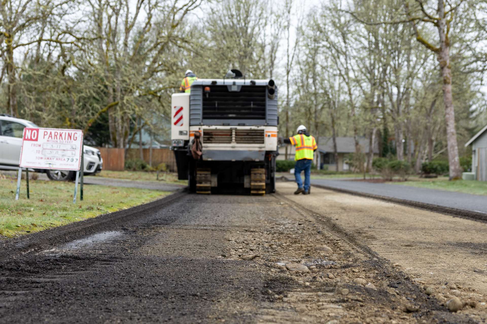 Asphalt milling in progress with PR Systems machinery and workers maintaining roadway in suburban area.
