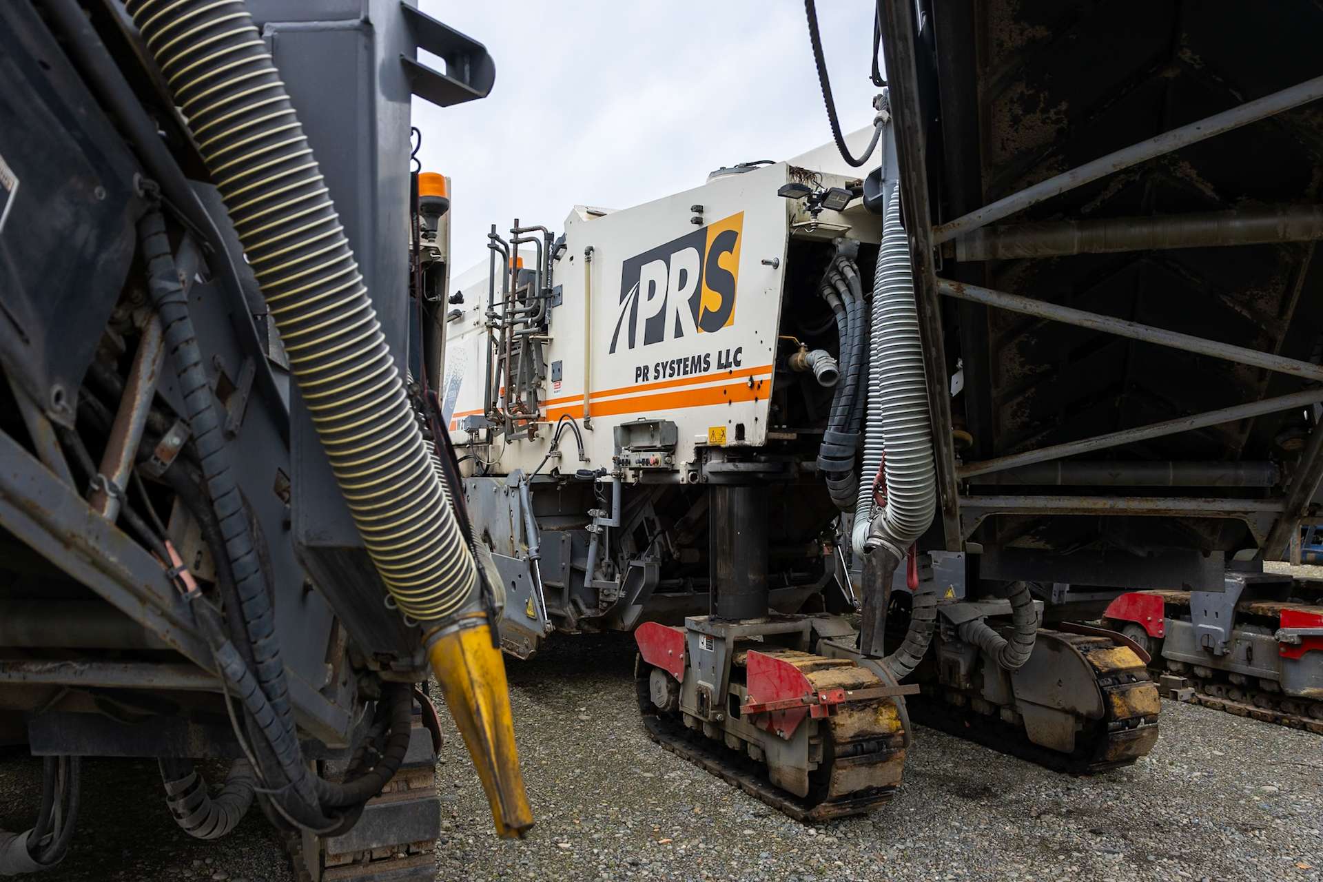 Close-up of PR Systems Wirtgen milling equipment with visible hydraulic lines and tracked undercarriage.