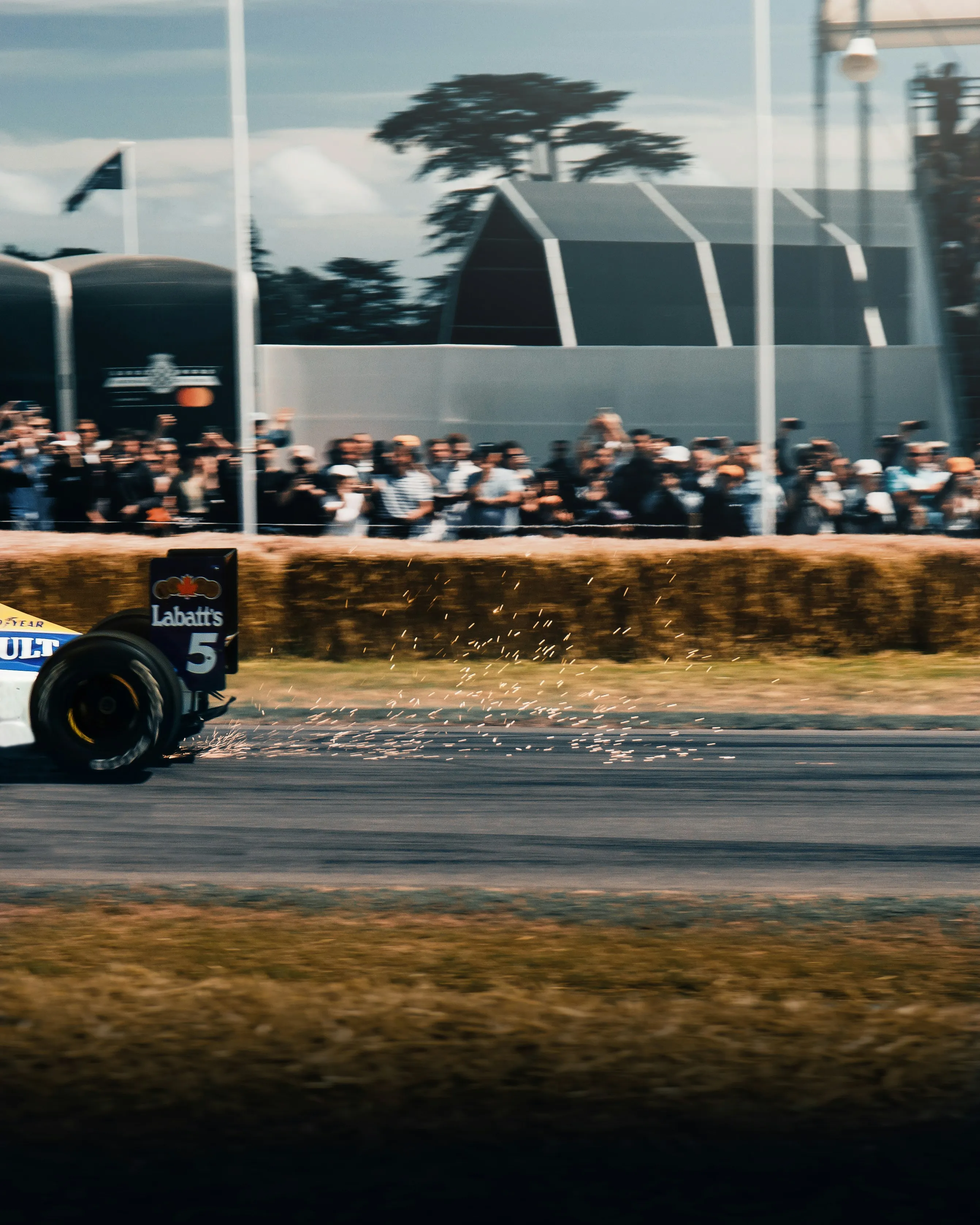 Parte trasera de un coche de carreras lanzando chispas en una pista frente a una multitud de espectadores.