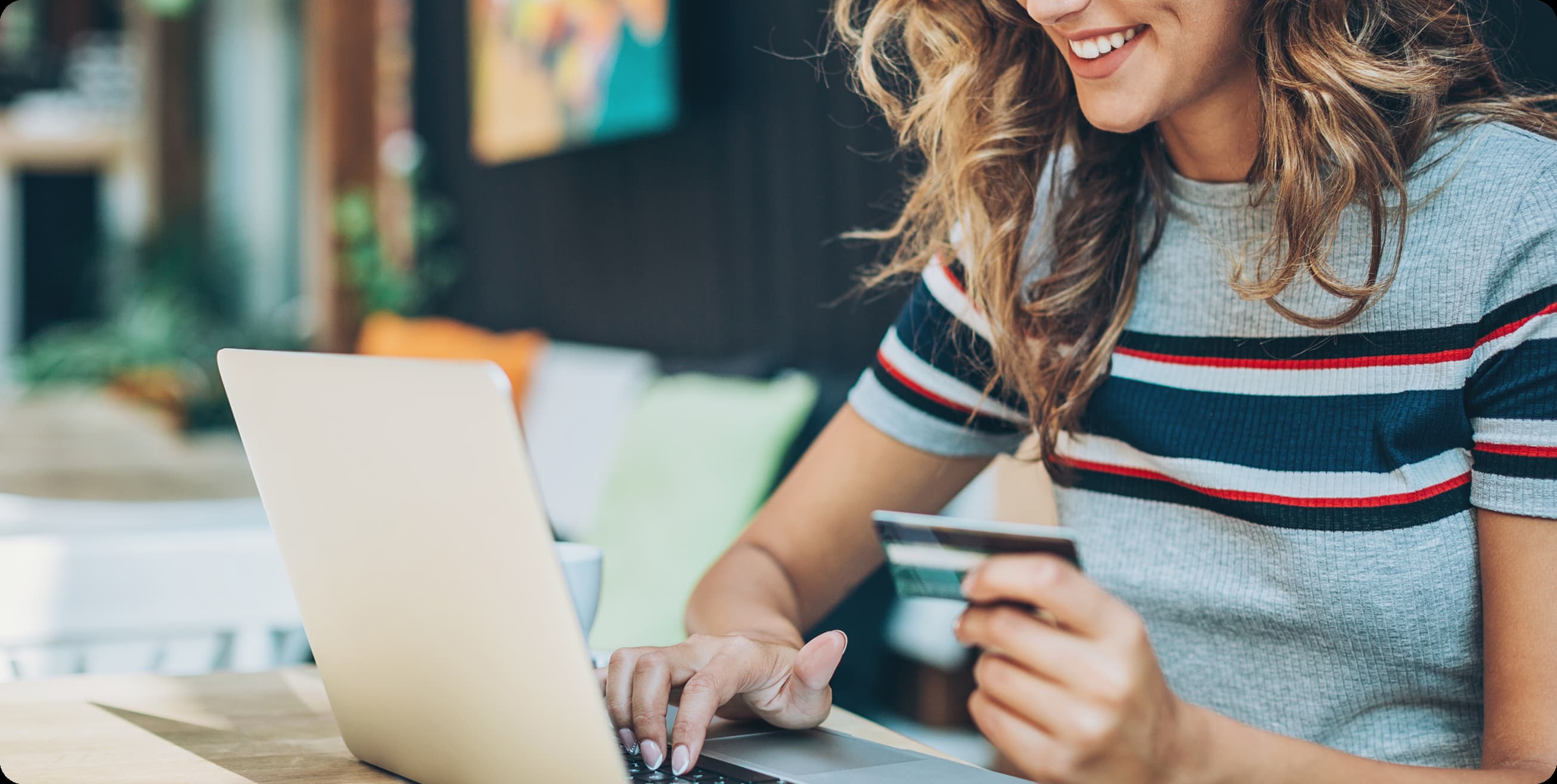 Smiling woman with curly hair holding a credit card while using a laptop