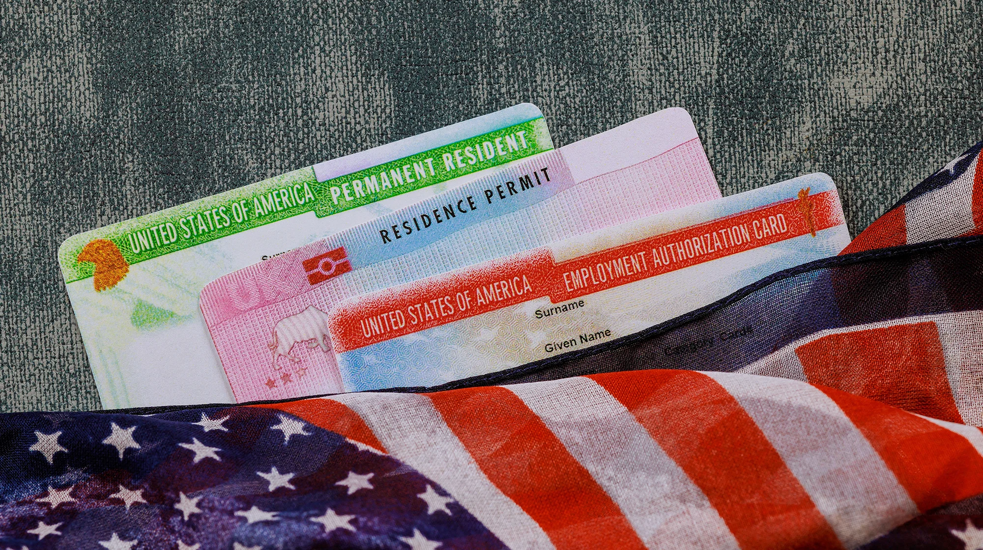 Image of a green card and work authorization card under a US flag.