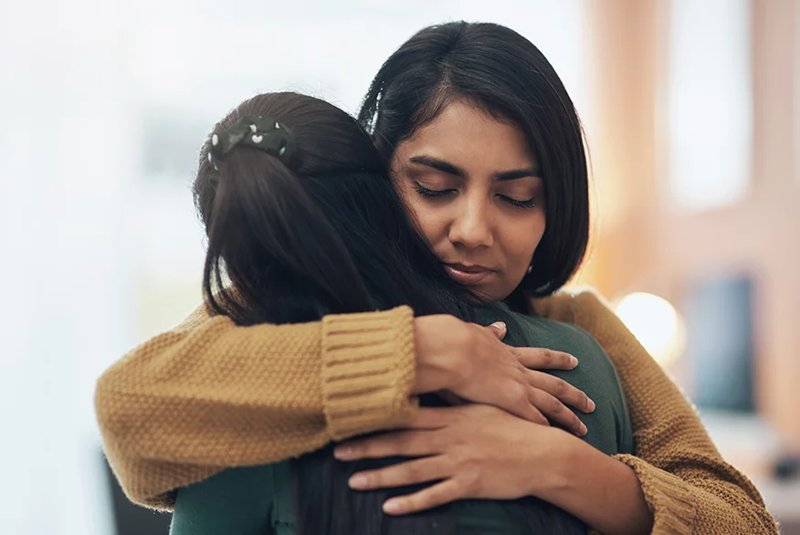 A sad woman hugs another one.