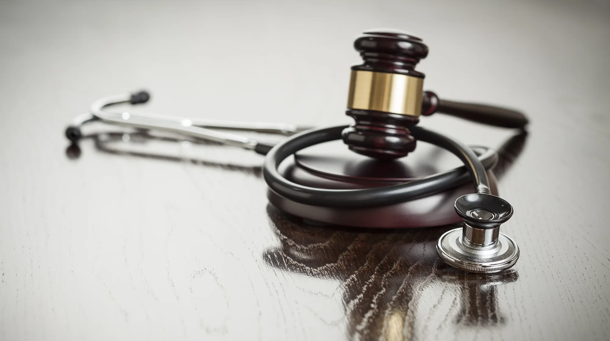 Gavel and Stethoscope on Reflective Wooden Table.