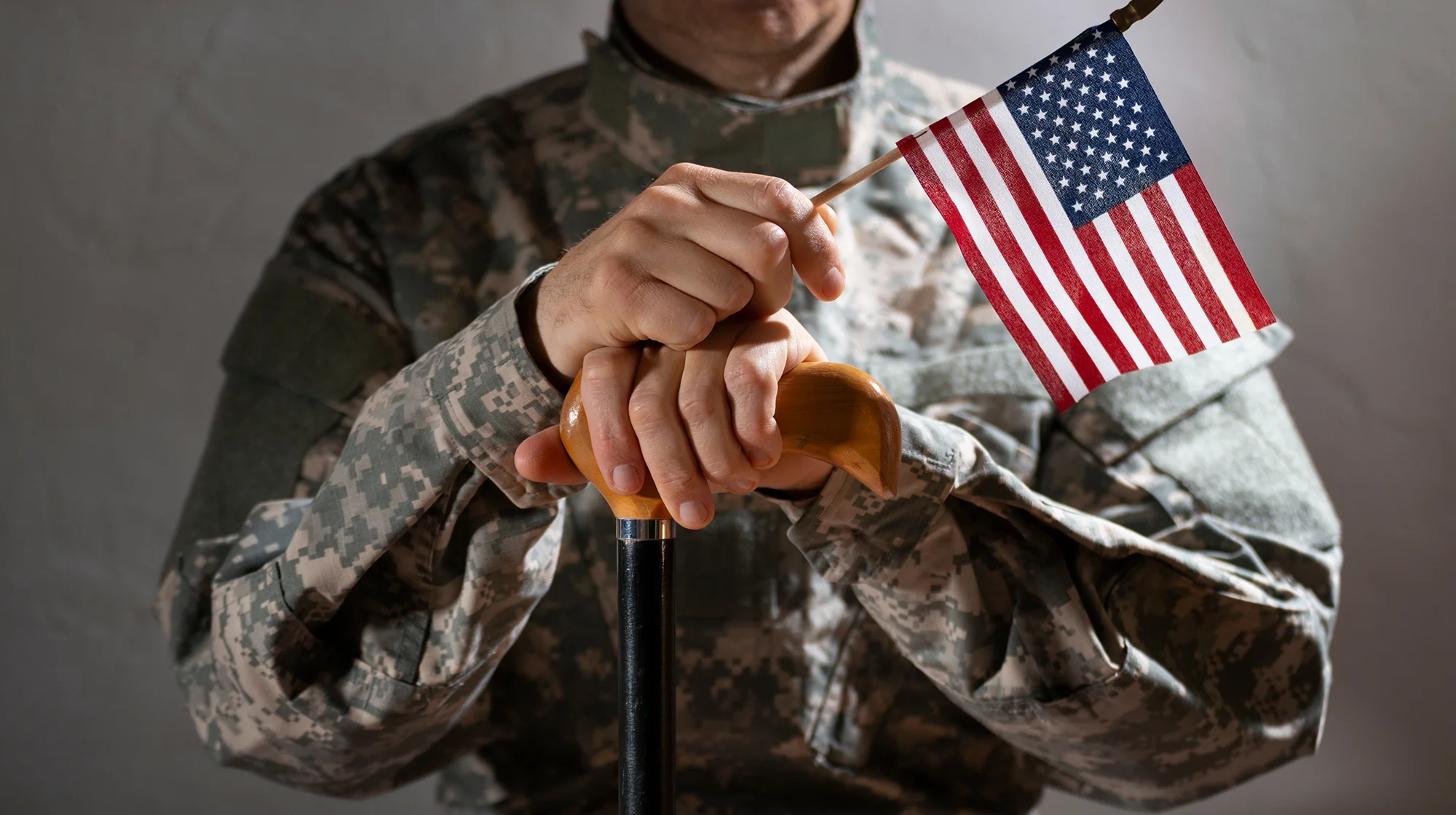 Soldier in camouflage uniform holding a cane and us flag symbolizing veteran support and resilience