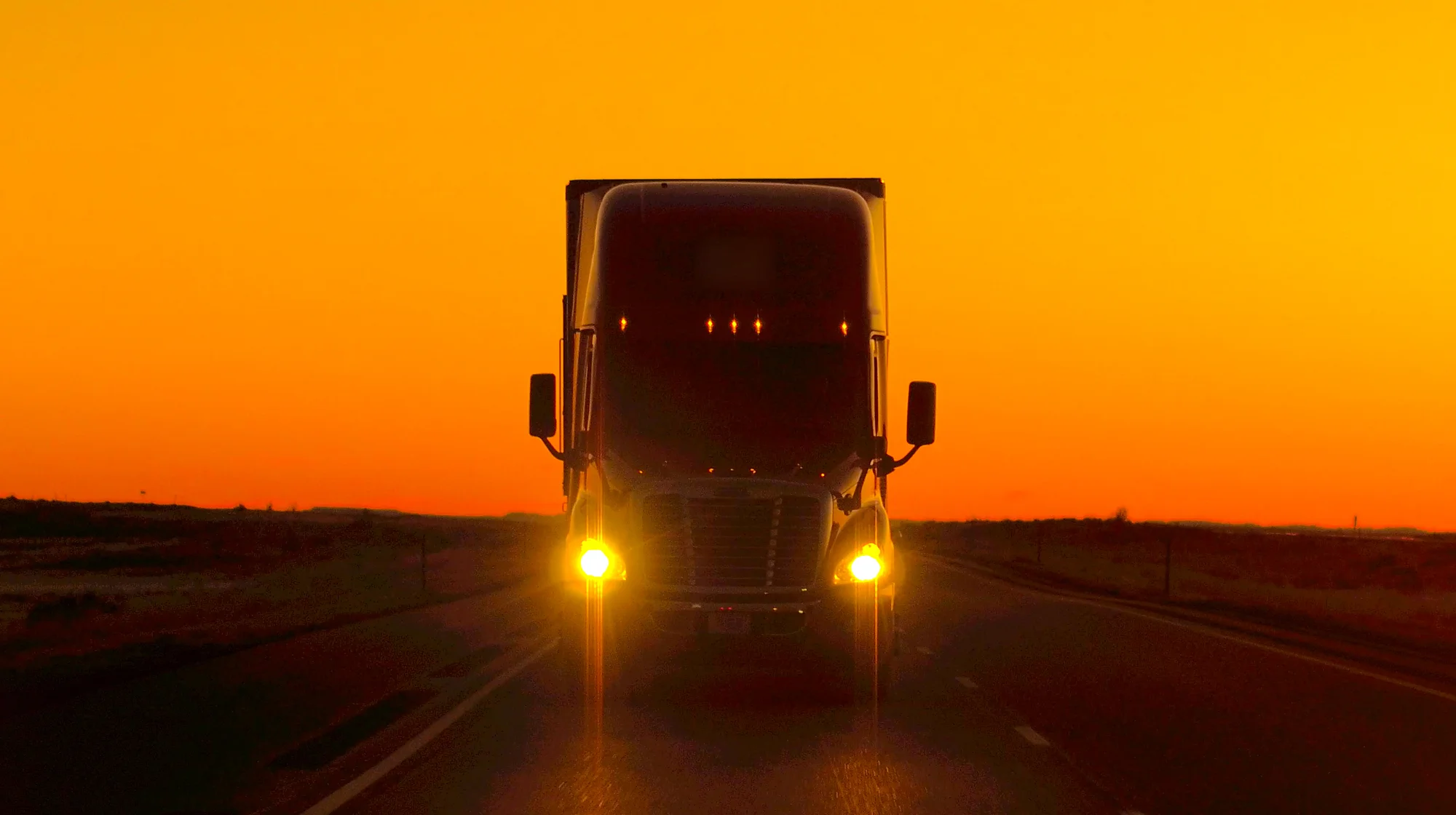 A semi truck driving on the road at the sunset.