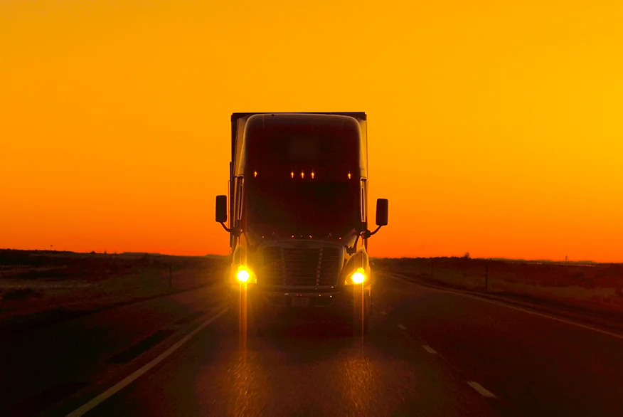 A semi truck driving on the road at the sunset.