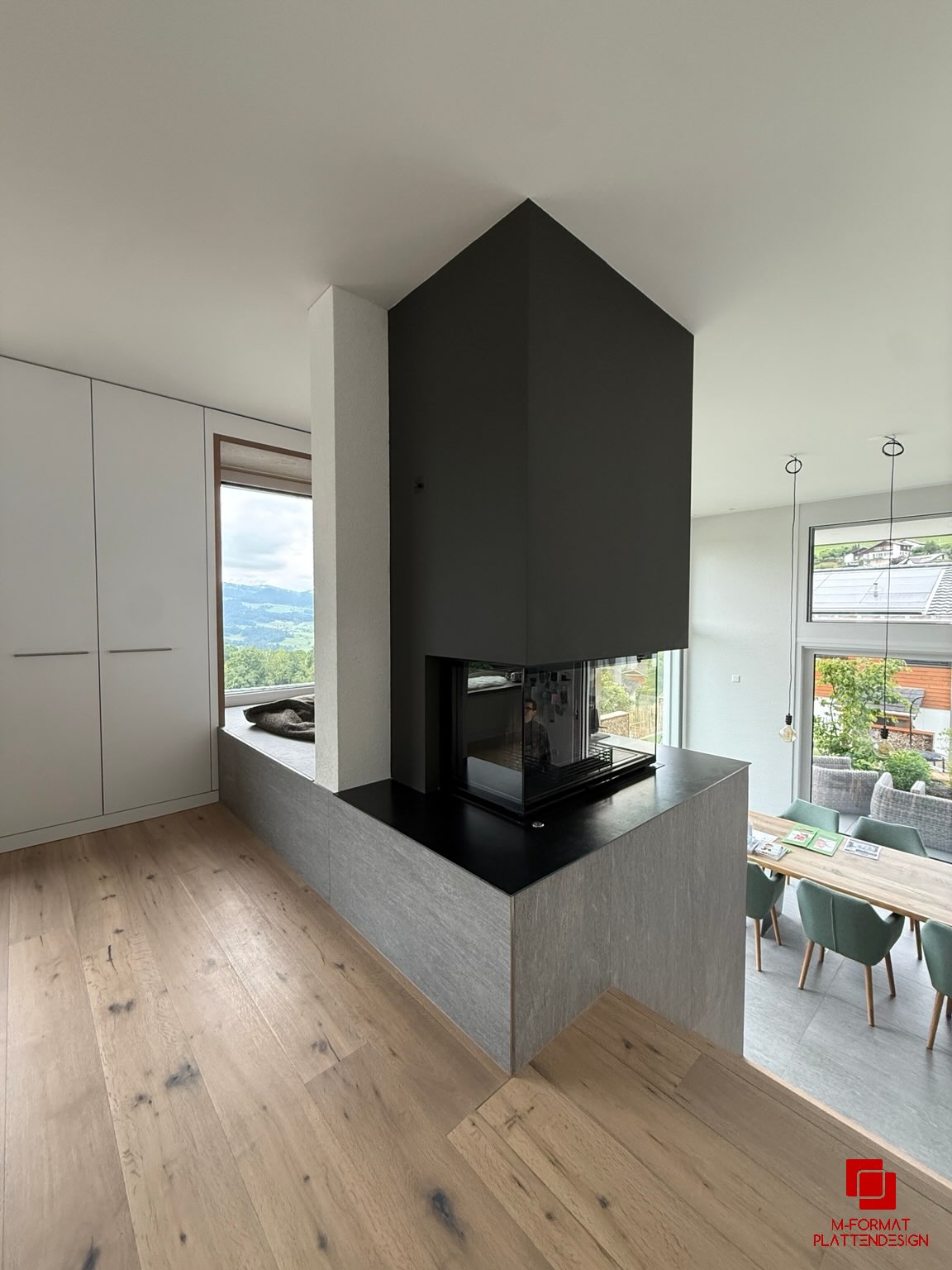 Modernes Cheminée mit grauer Plattenverkleidung, schwarzer Abdeckung und angrenzender Holztreppe