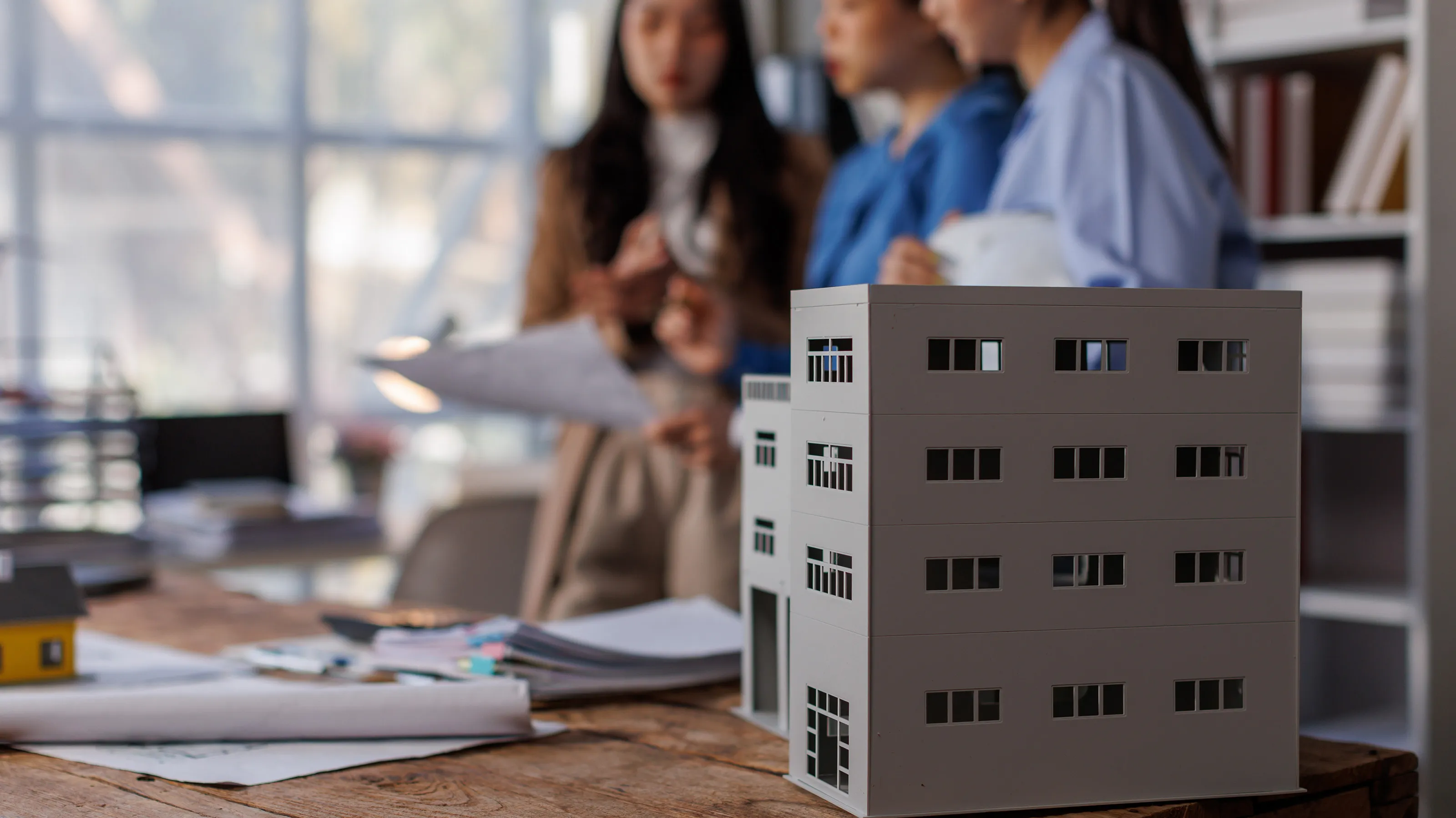 A business meeting of a real estate engineering team reviewing a blueprint for a construction project as a well as a model of the project