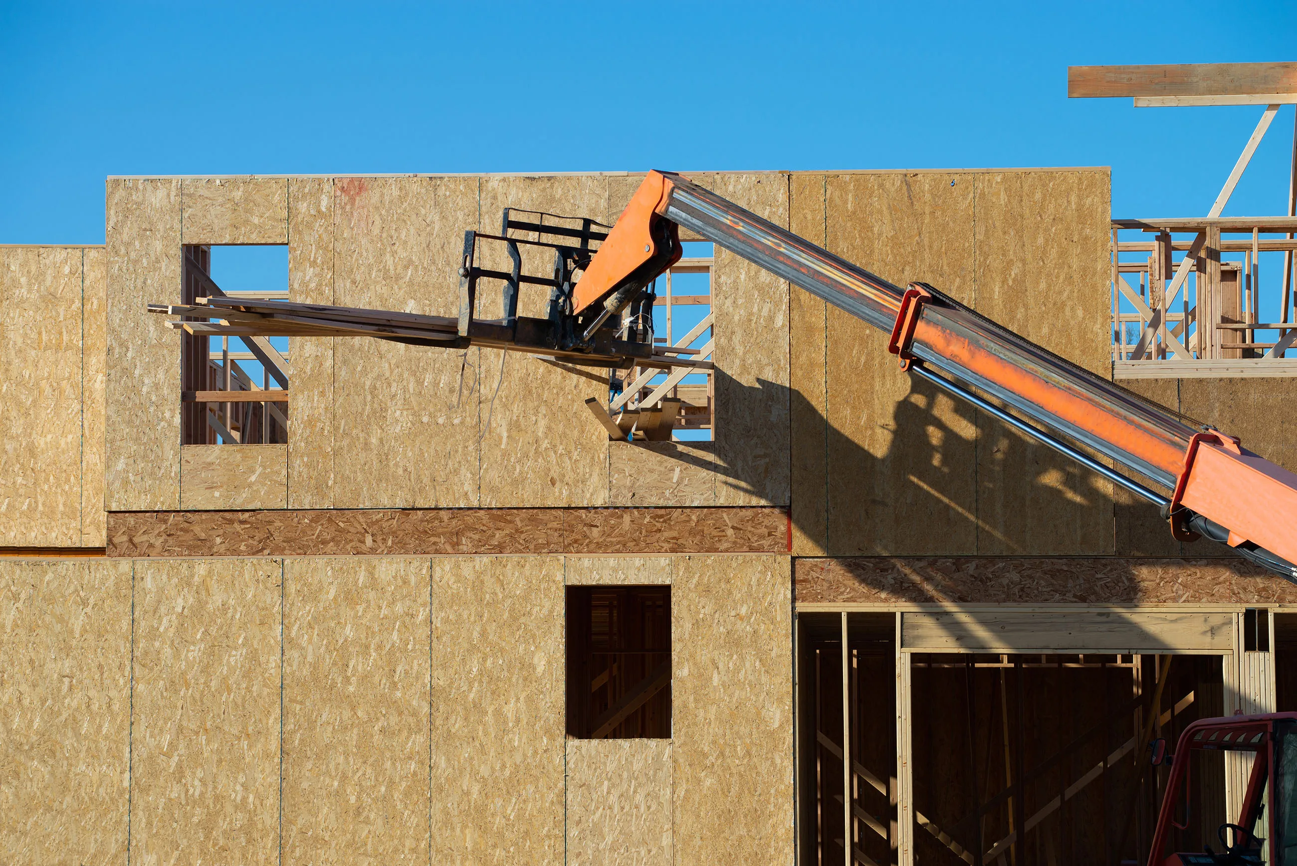 Forklift at a construction site of a plywood house with new wood frame wall