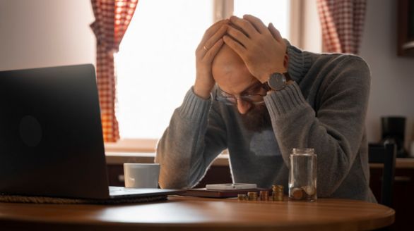 Un homme assis à une table, la tête dans les mains, semblant préoccupé ou accablé.