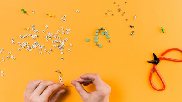 Des mains tenant des ciseaux sur un fond jaune, avec une paire de ciseaux posée à côté.