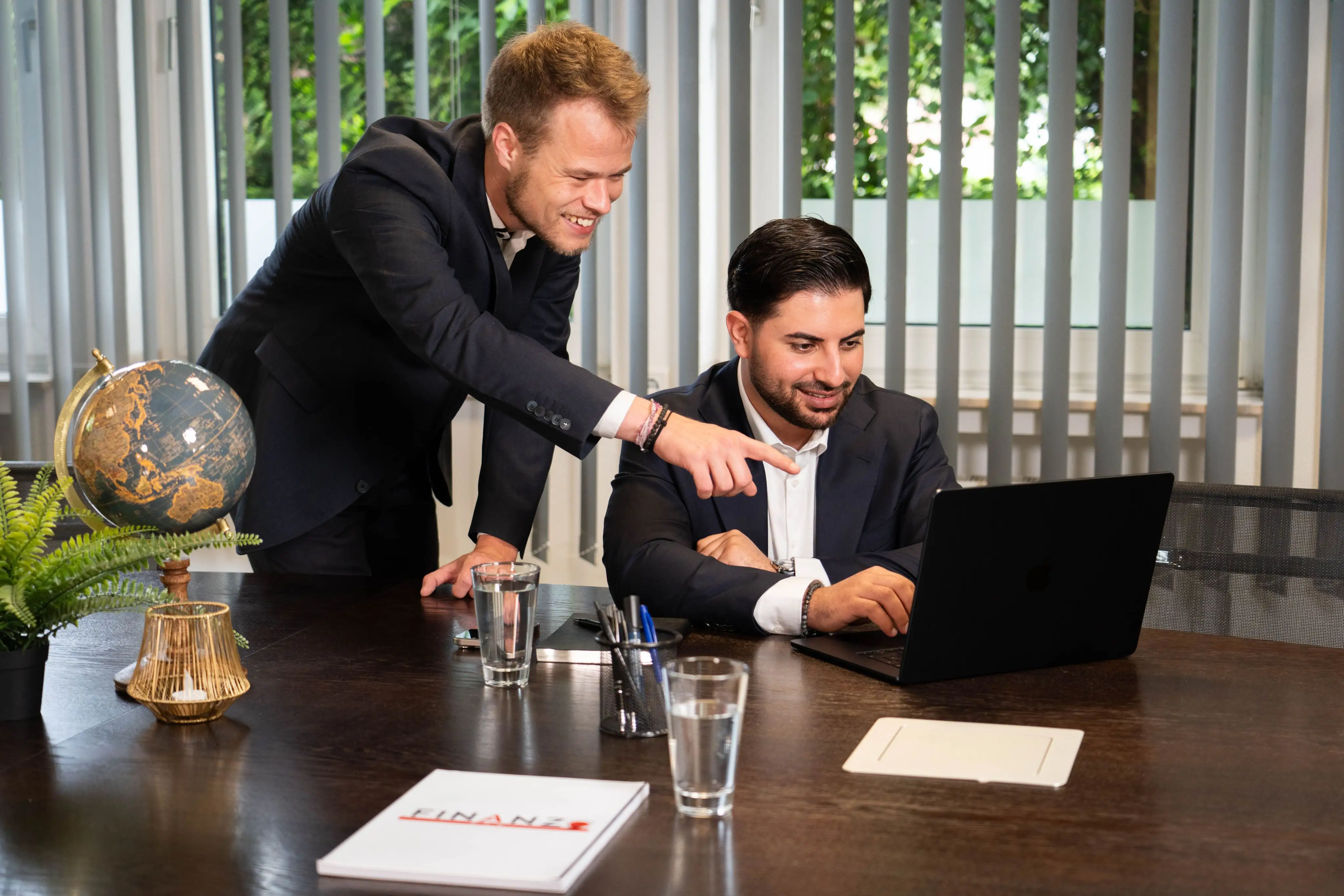 Tim und Nasim vor einem Laptop zur Besprechung einer Finanz-Strategie in ihrem Büro.