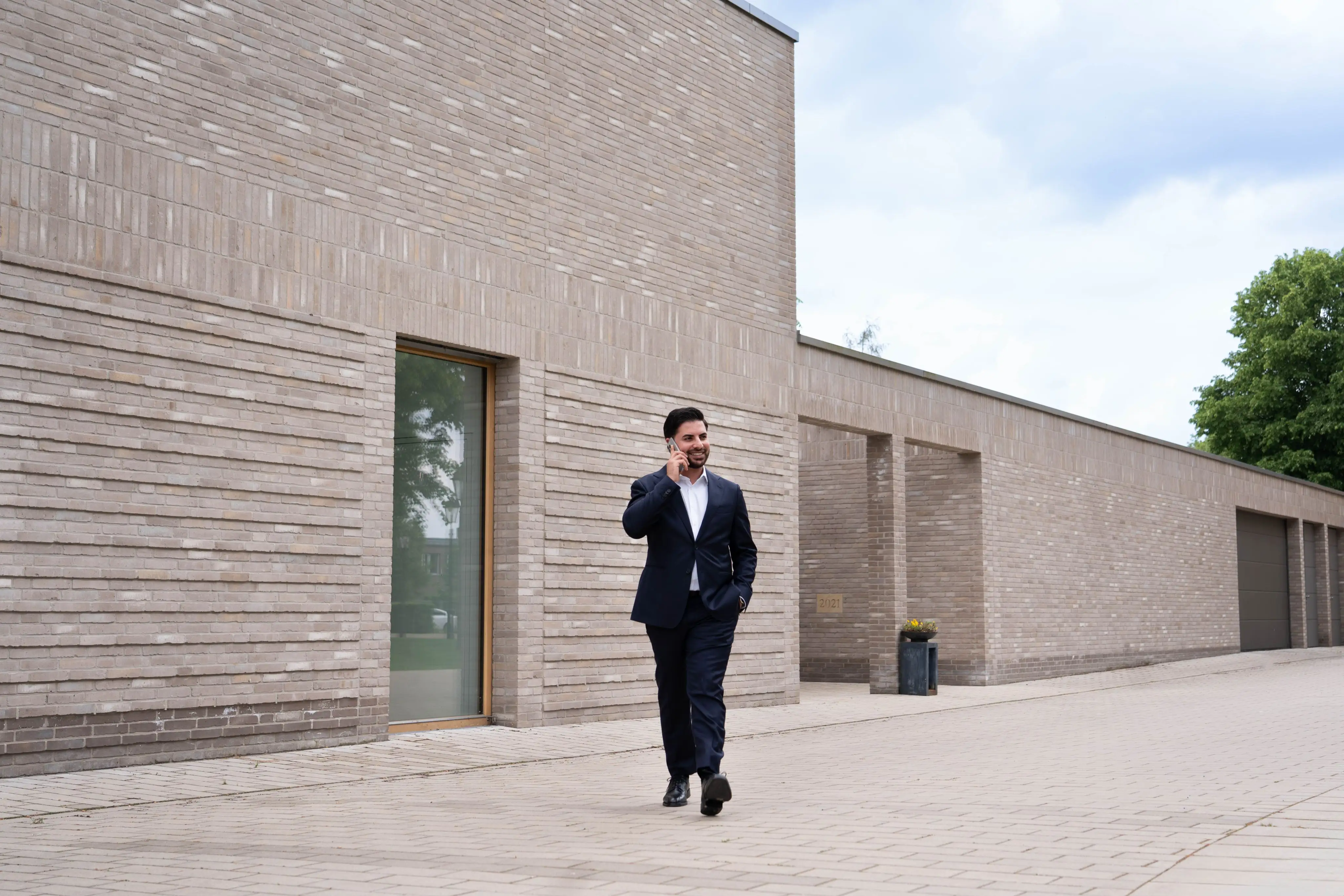 In der Mitte des Bildes geht Nasim Birawi vor einem grauen neuen Gebäude.