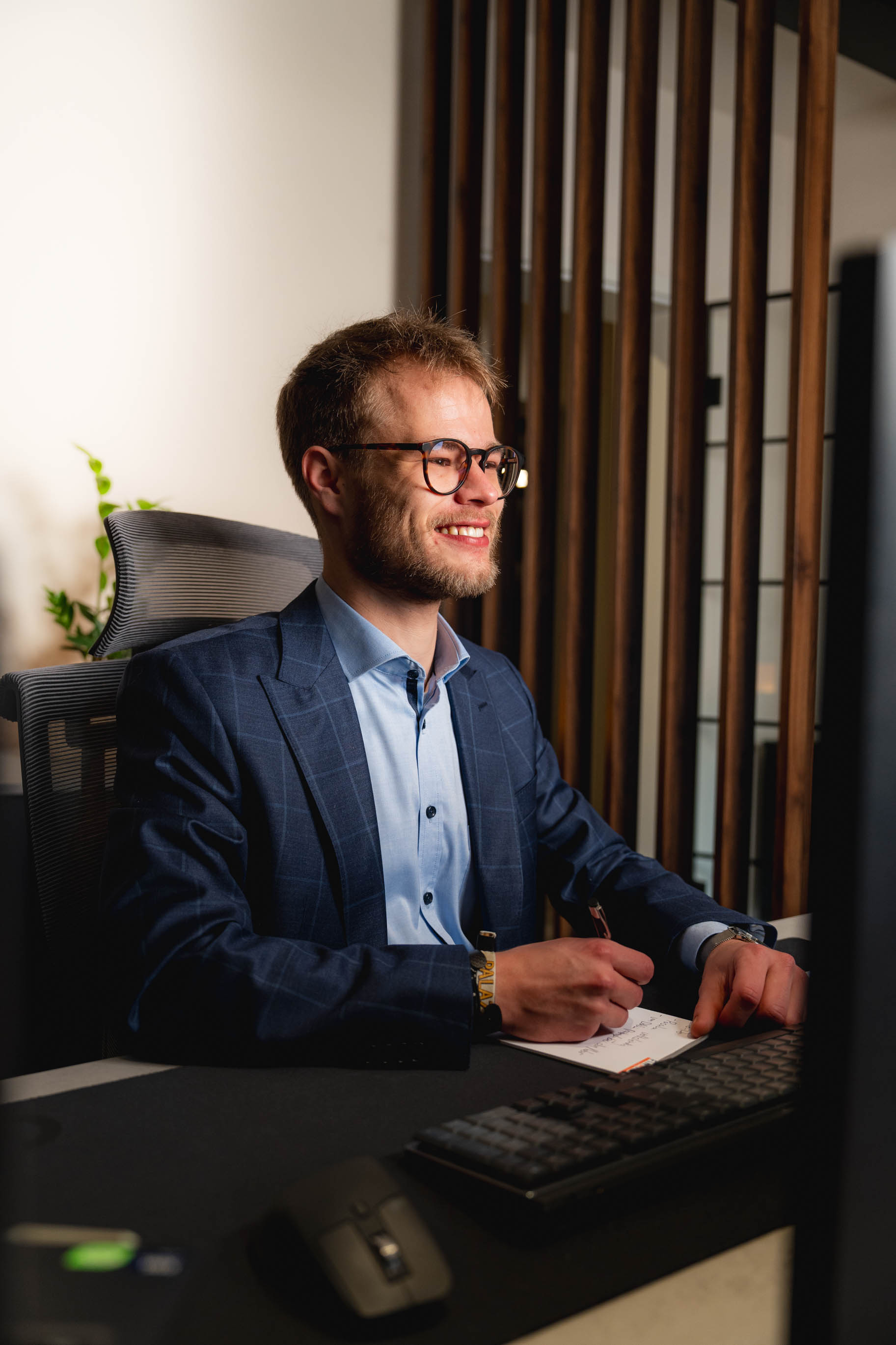 Tim sitzt am Schreibtisch und schreibt Notizen, vor einem Computerbildschirm.