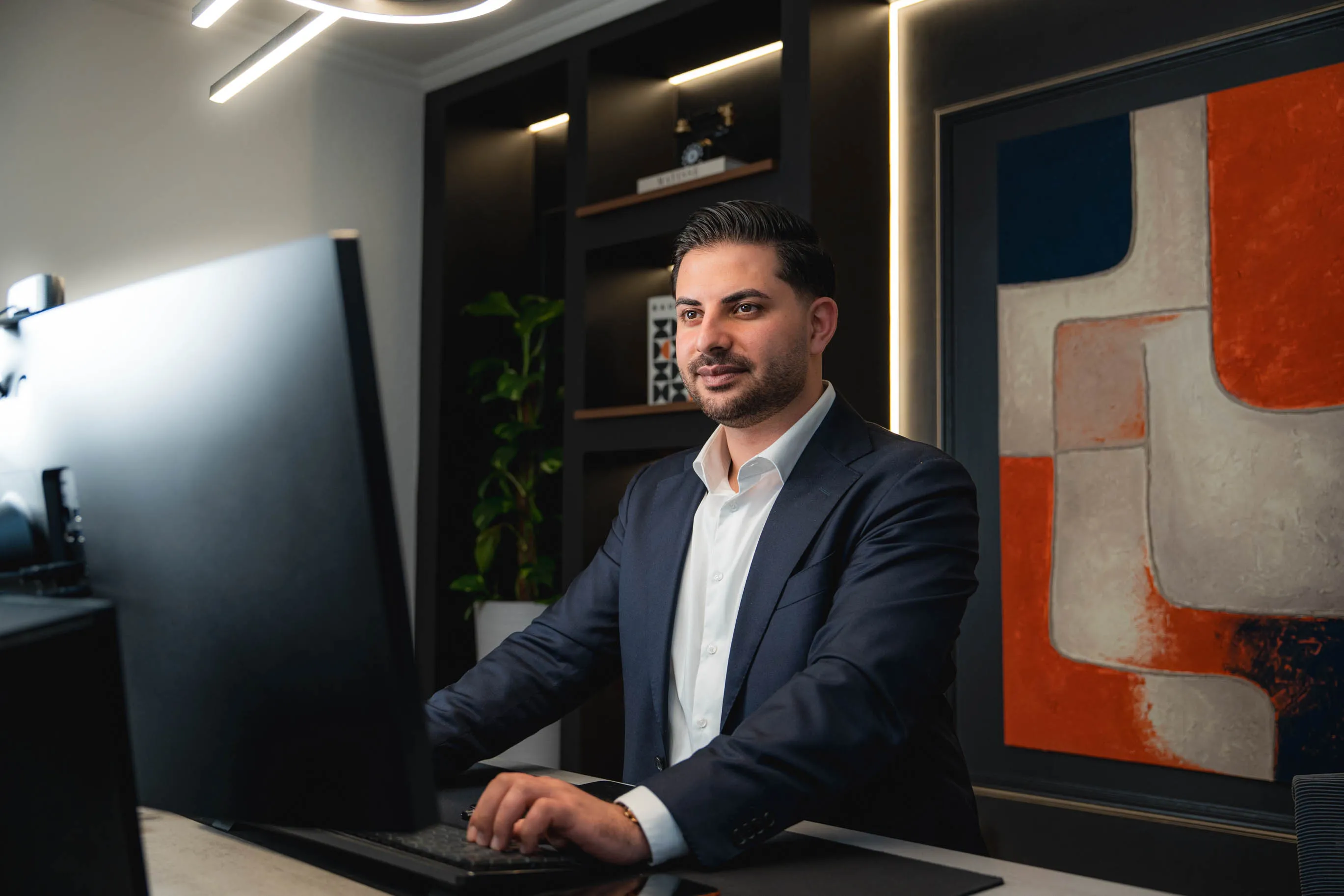 Nasim arbeitet konzentriert an einem Computer in einem modernen Büro mit abstraktem Kunstbild im Hintergrund.