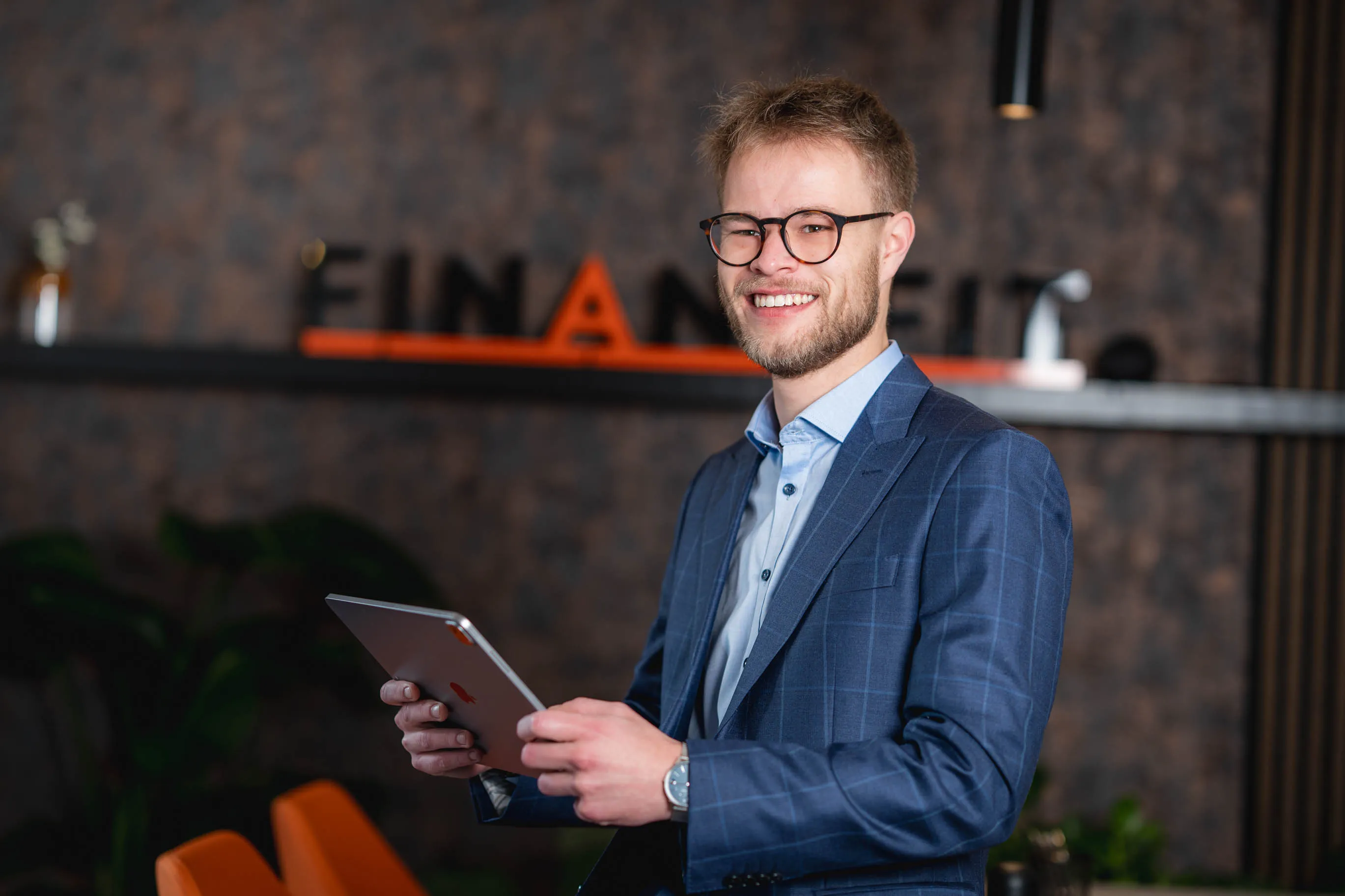 Tim hält ein Tablet und lächelt in einem modernen Büro.