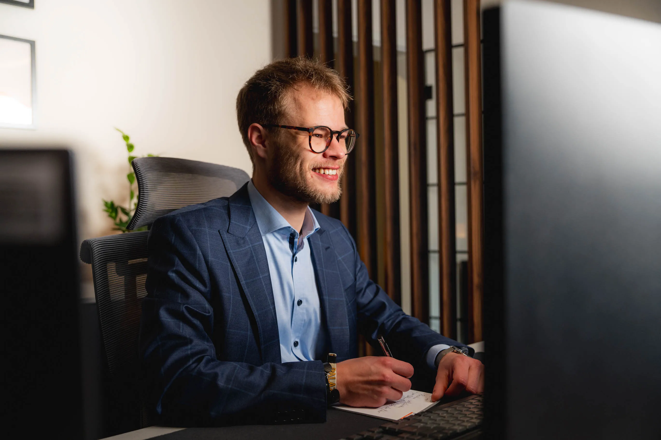 Tim lächelt, während er an einem Schreibtisch Notizen macht.