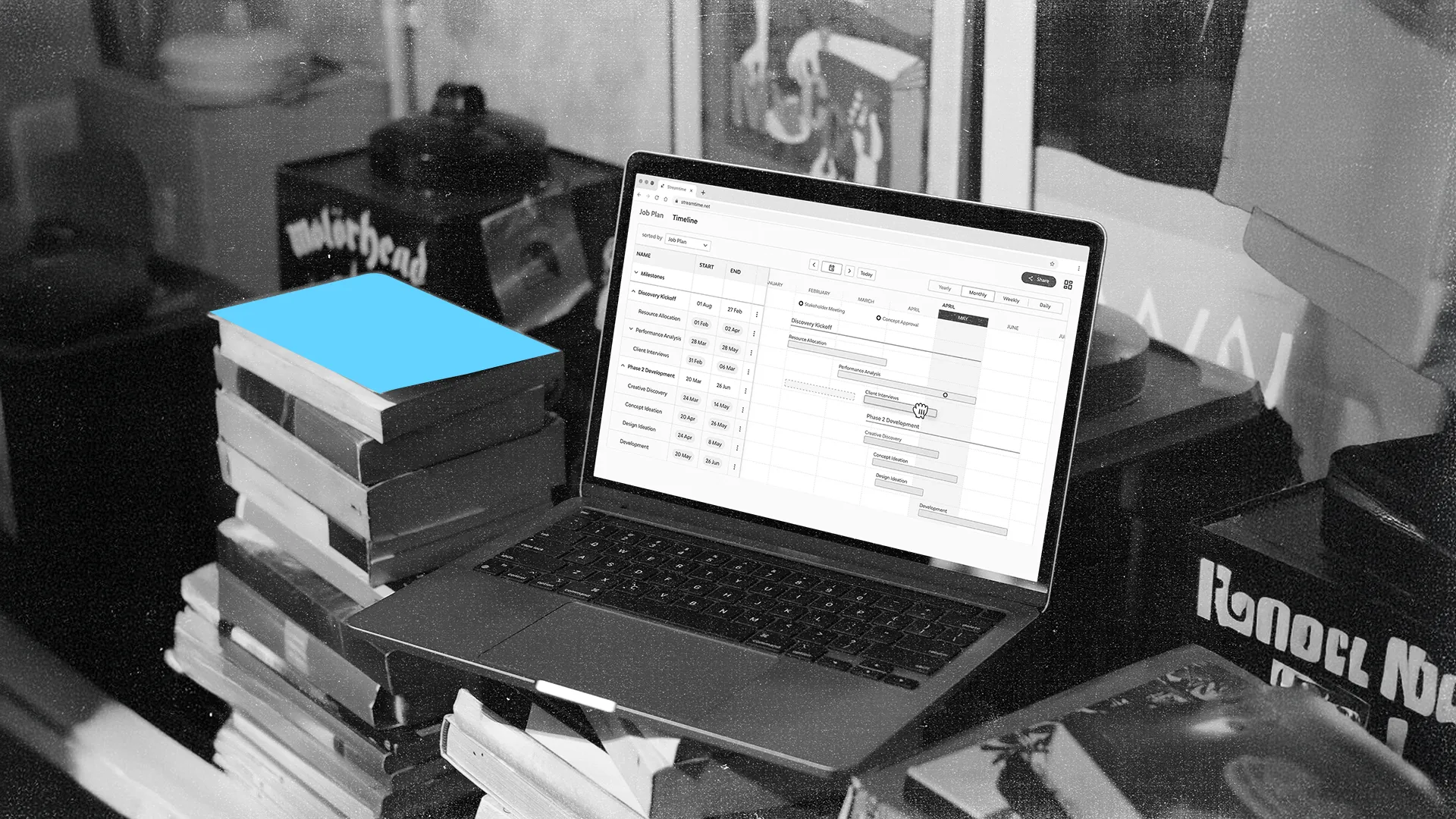 Open laptop on a stack of books showing a job plan timeline with tasks and dates.