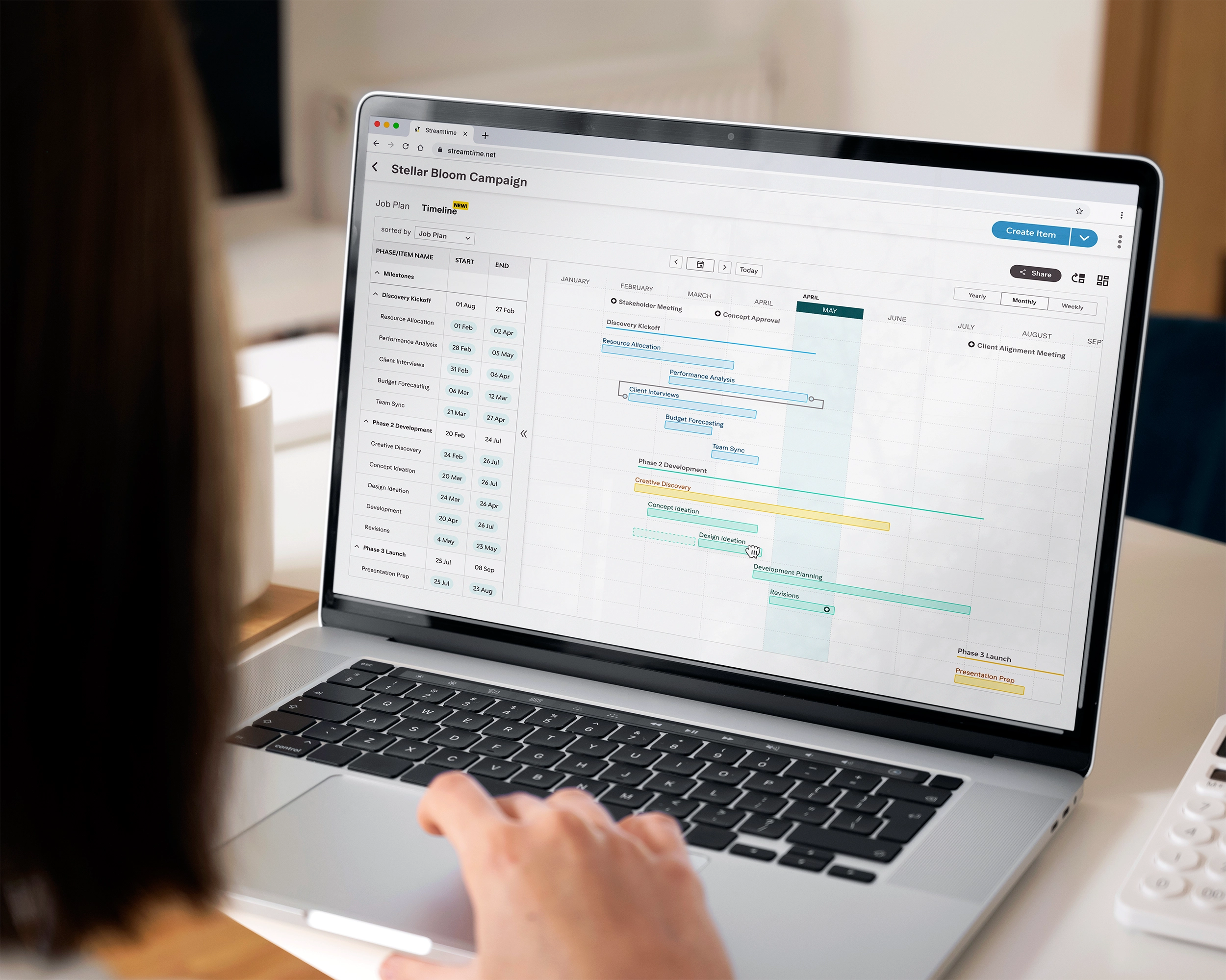 Person viewing a laptop displaying a project timeline for the Stellar Bloom Campaign with tasks, dates, and milestones laid out in a calendar format.