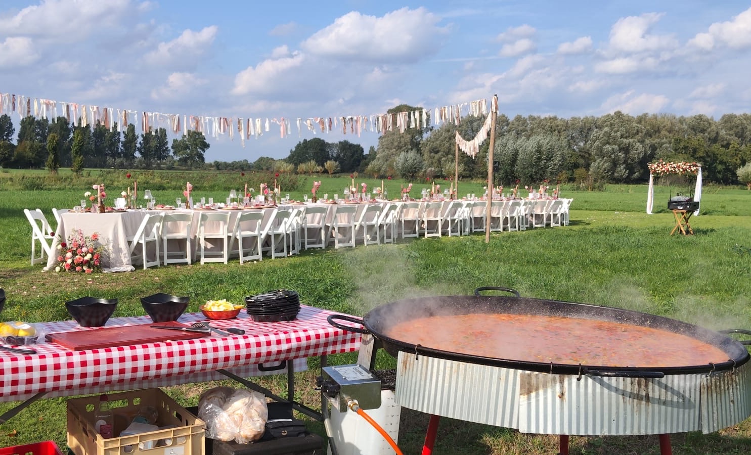 Gedekte trouwtafel in een weiland met een grote paellapan op de voorgrond, bruiloft in Veghel