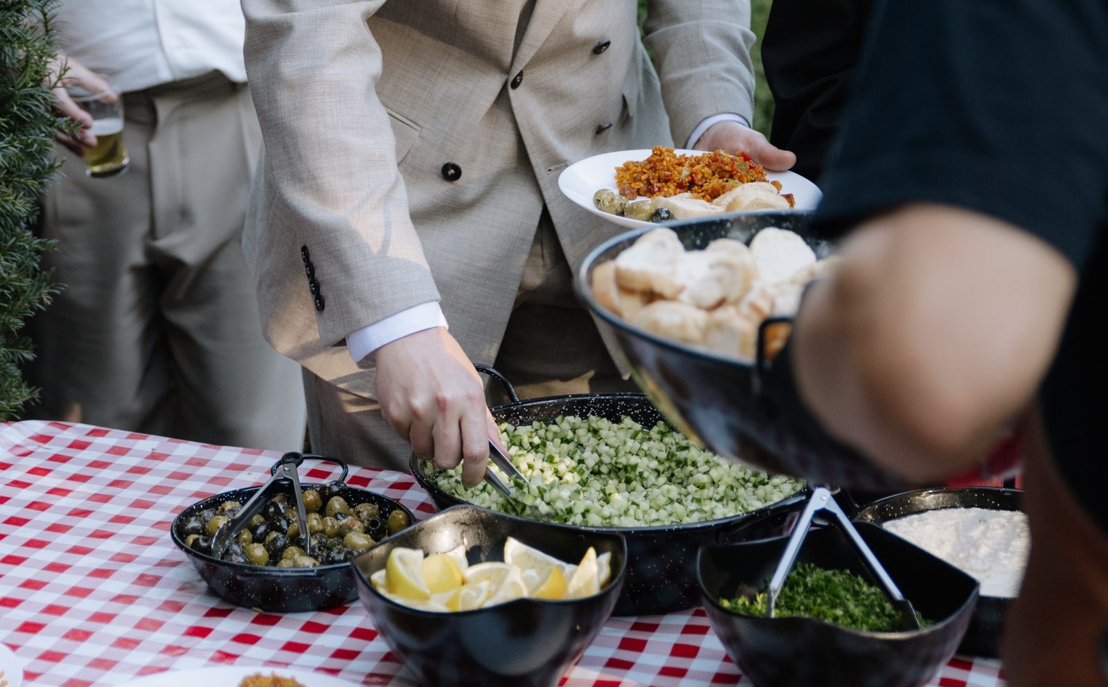 Gasten scheppen op aan de buffettafel met olijven, komkommersalade, brood en aioli