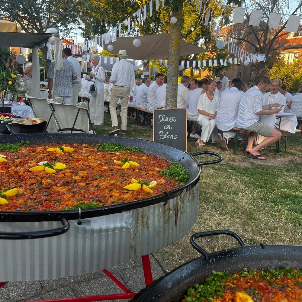 Twee paellapannen op een buurtfeest met lange tafels en gasten in het wit