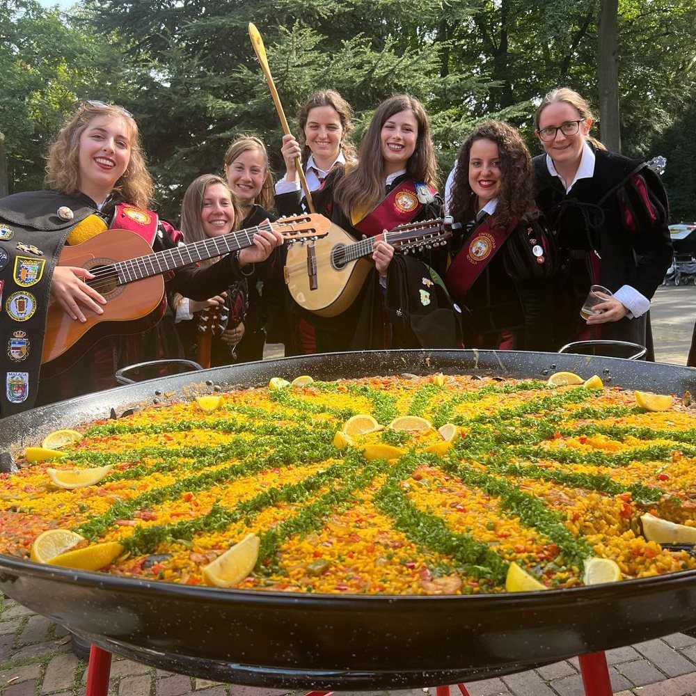 Studentes van een tuna met gitaar en mandoline achter een versierde paellapan