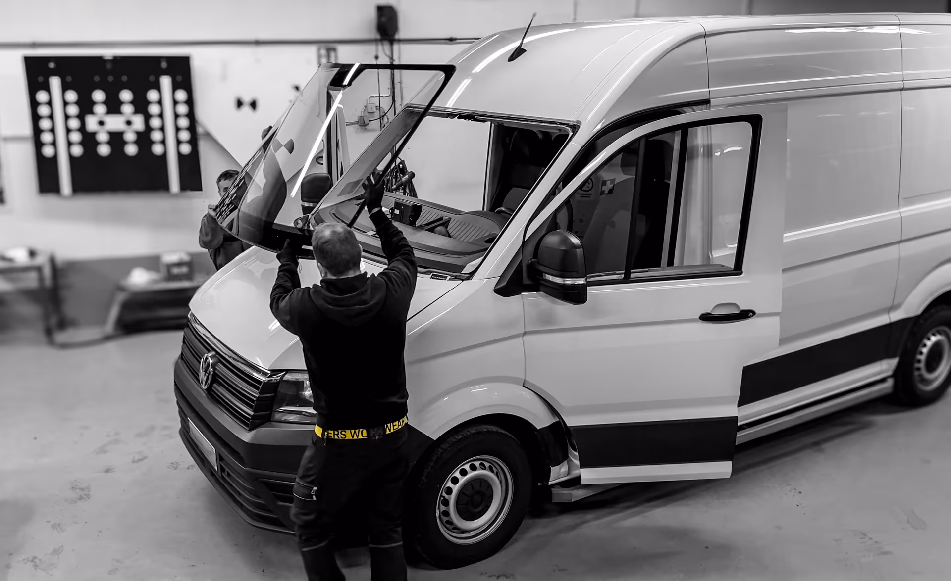 Kaksi miestä vaihtaa pakettiautoon tuulilasia