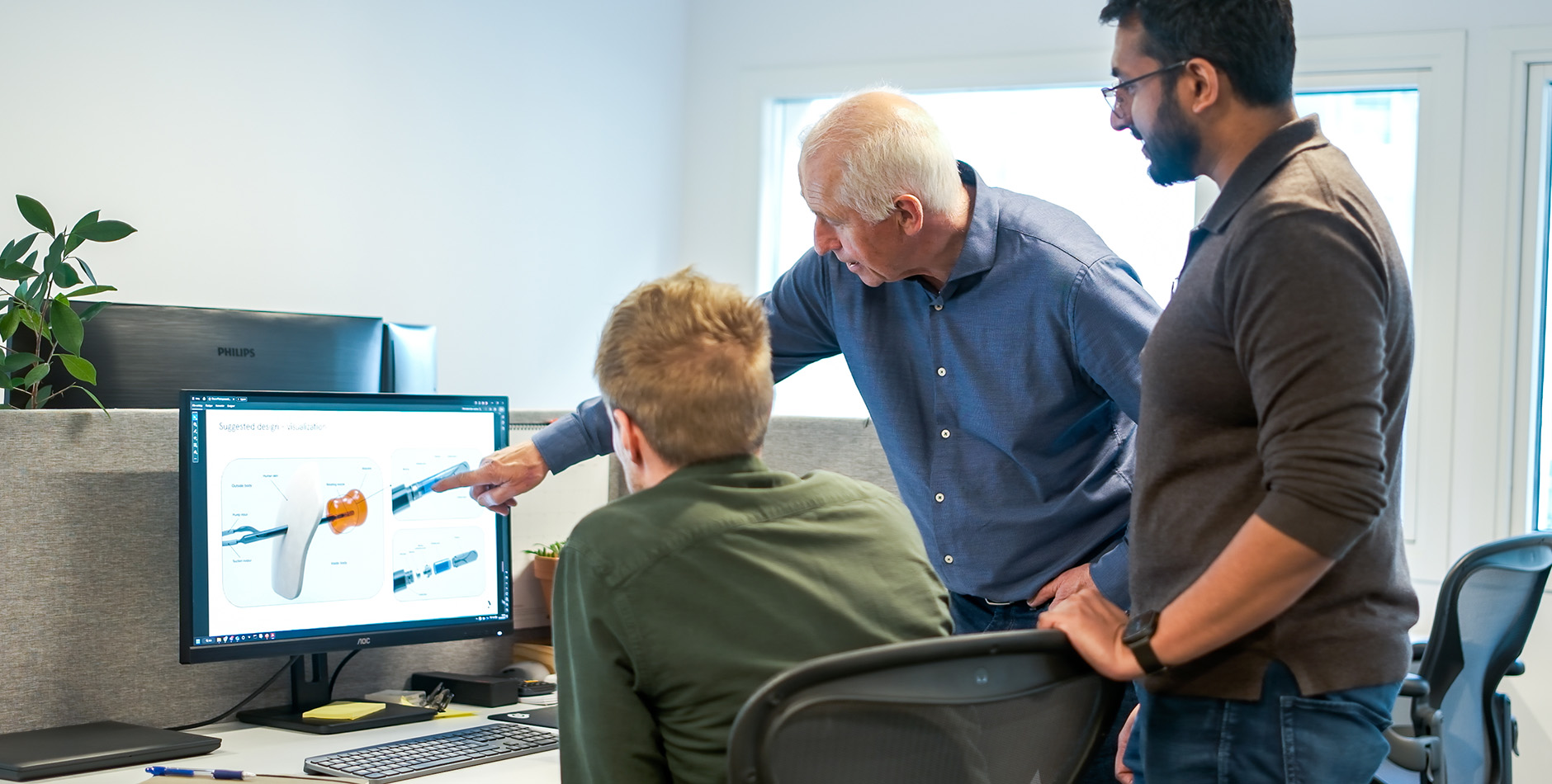 Three men standing in front of a computer screen