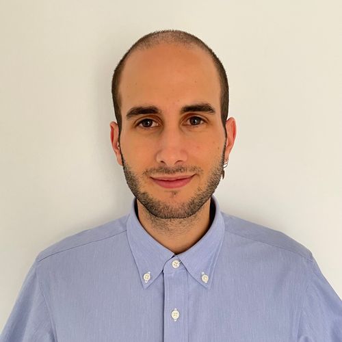 Smiling man with short dark hair, beard, and blue button-up shirt against a plain white background.