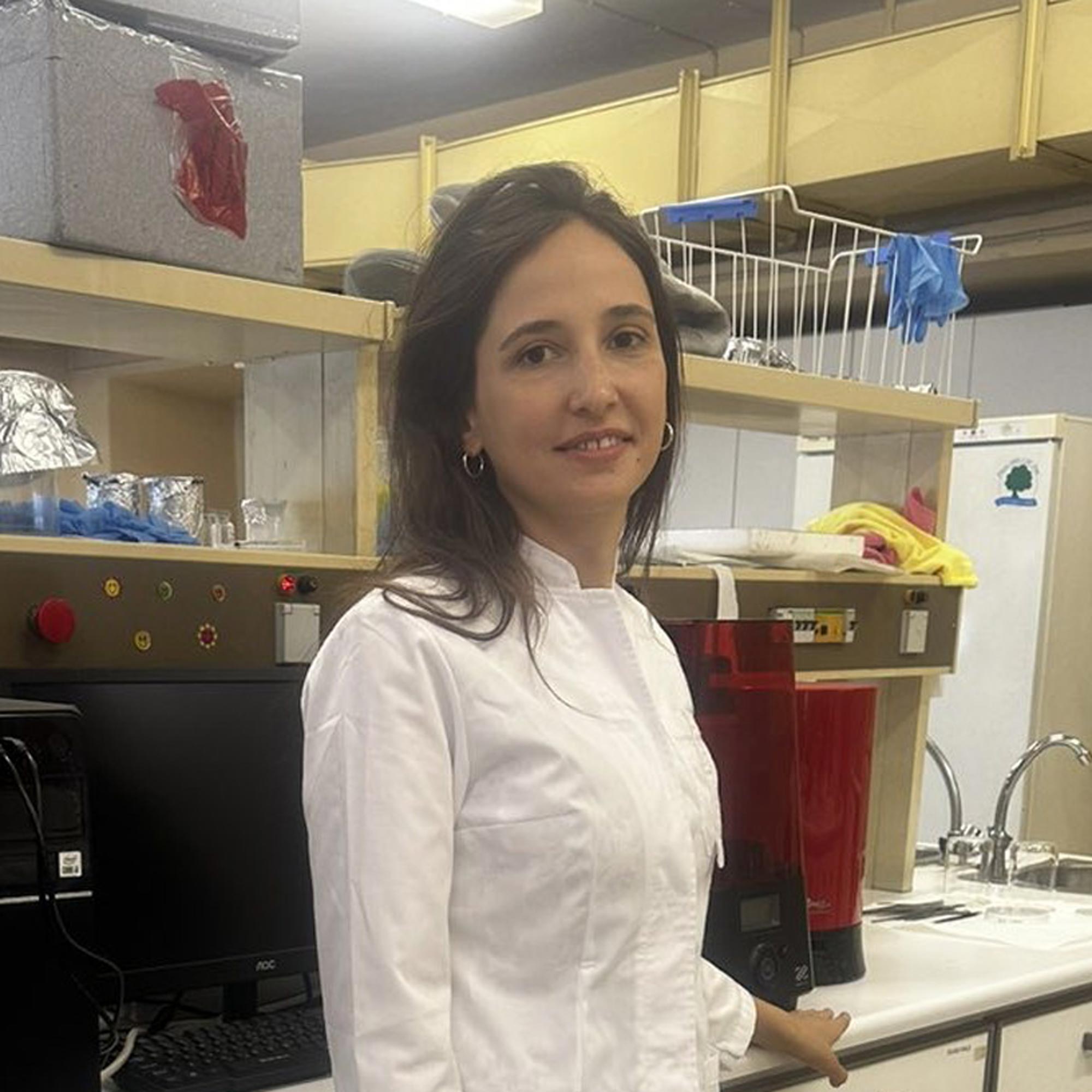 Woman in a white lab coat standing in a laboratory with scientific equipment and computer.