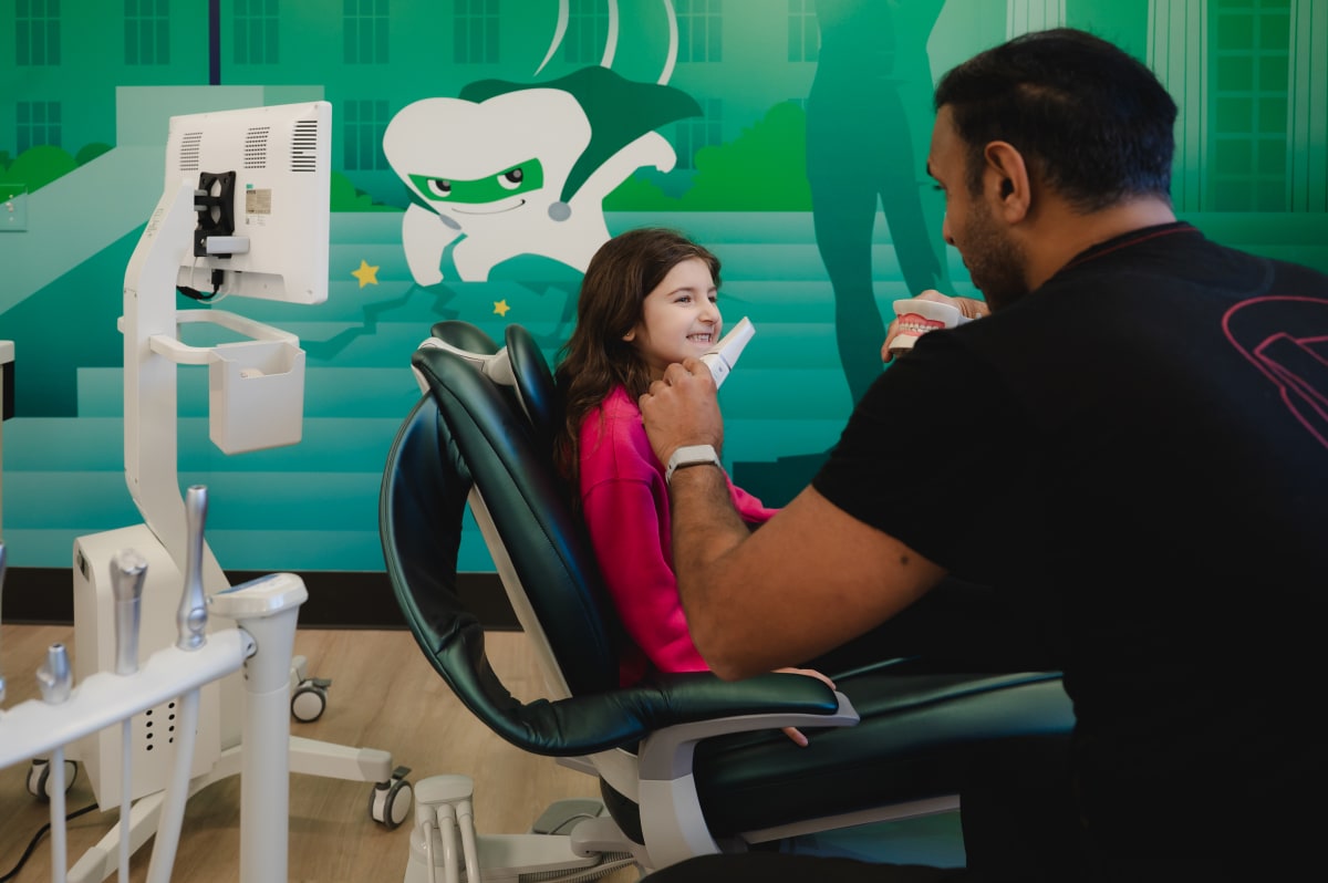 Pediatric dentist examining a young child in dental chair with green operatory