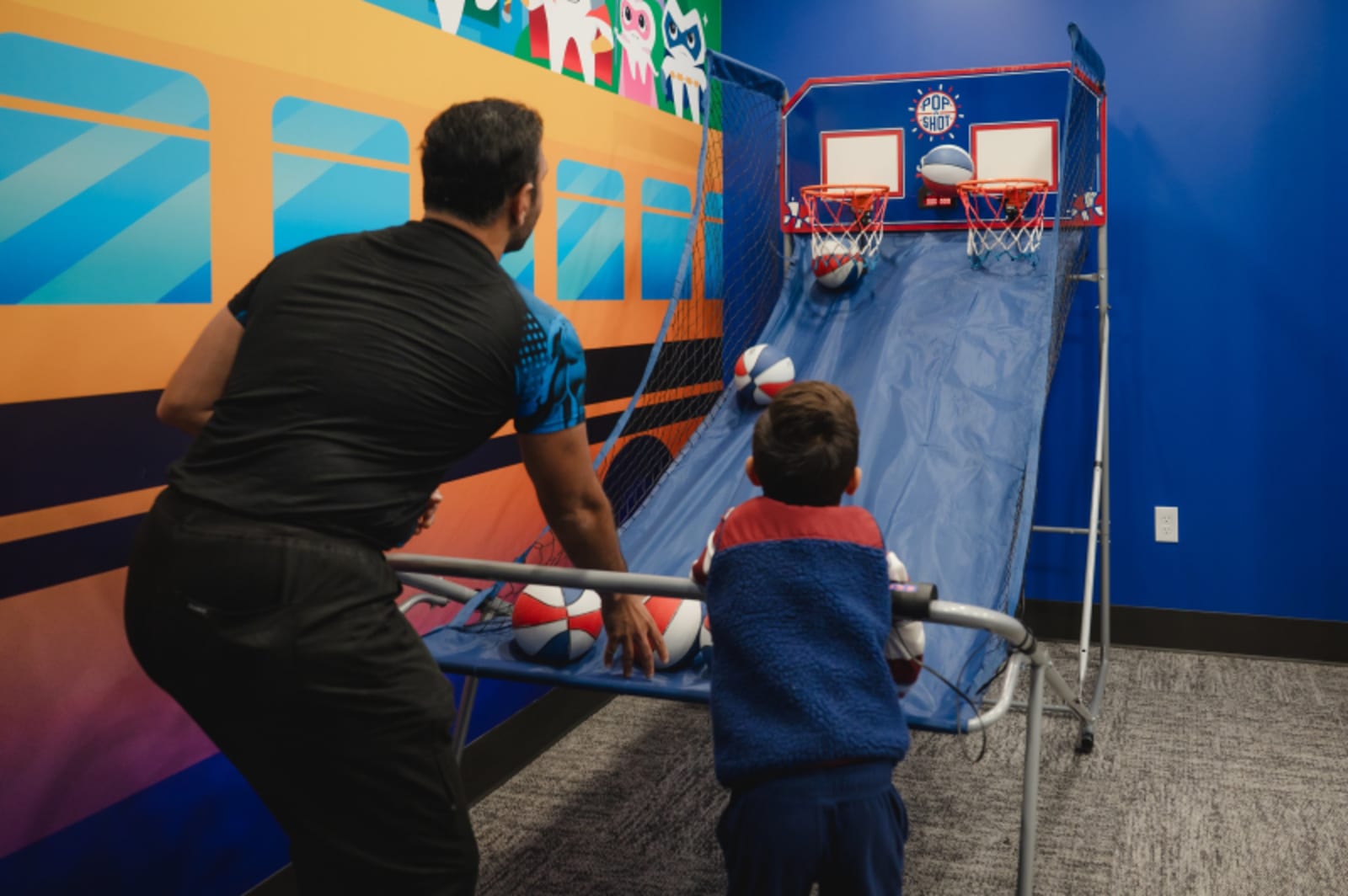 Pediatric dentist demonstrating dental equipment to a young patient in a colorful treatment room.