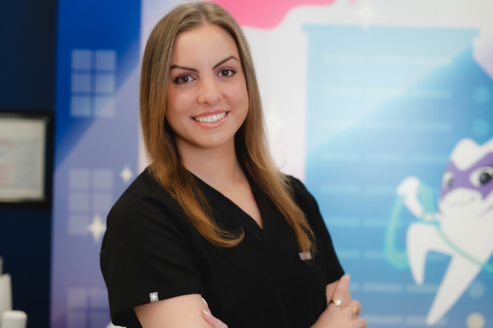 Female dentist smiling at camera in front of colorful practice mural and branding