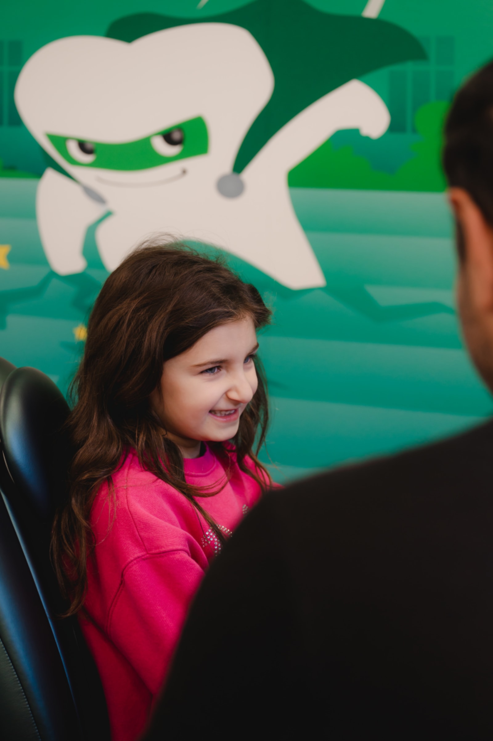 Young girl smiling in dental chair with dentist during appointment at pediatric practice.