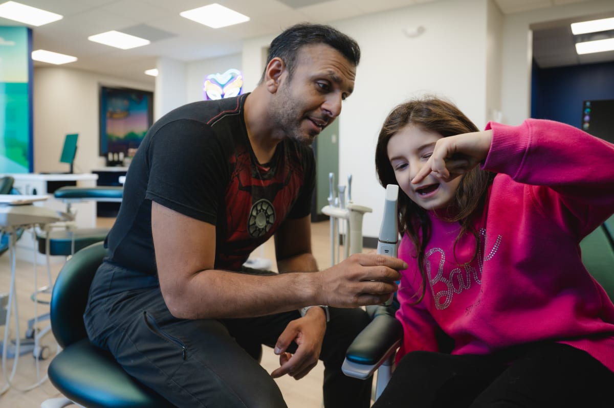 Pediatric dentist examining a young patient in treatment chair with colorful office walls