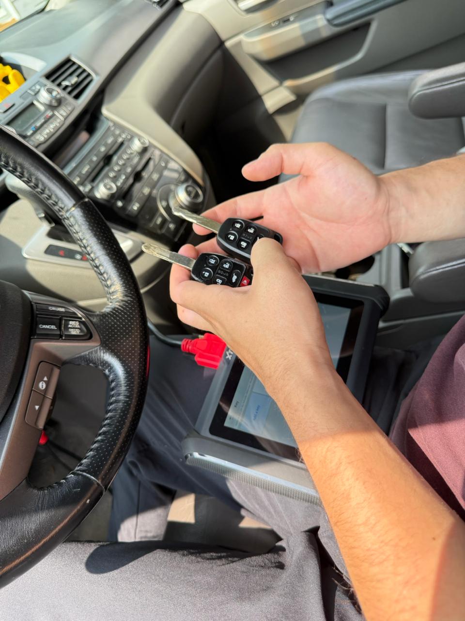 Locksmith holding two car keys and a diagnostic tool inside vehicle