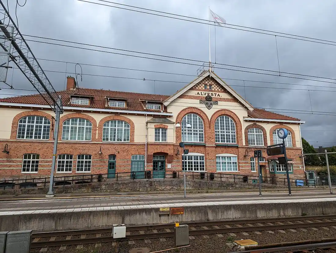 Stationshus i Alvesta med järnvägsspår och molnig himmel