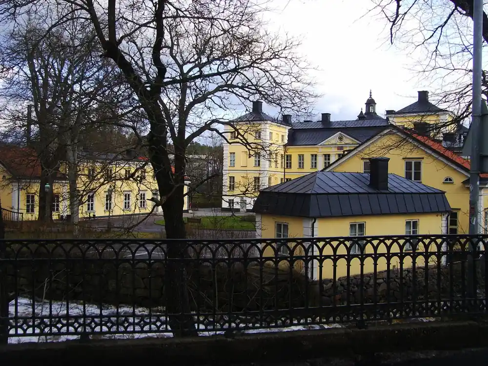 Större byggnad i Finspång bakom träd och räcke