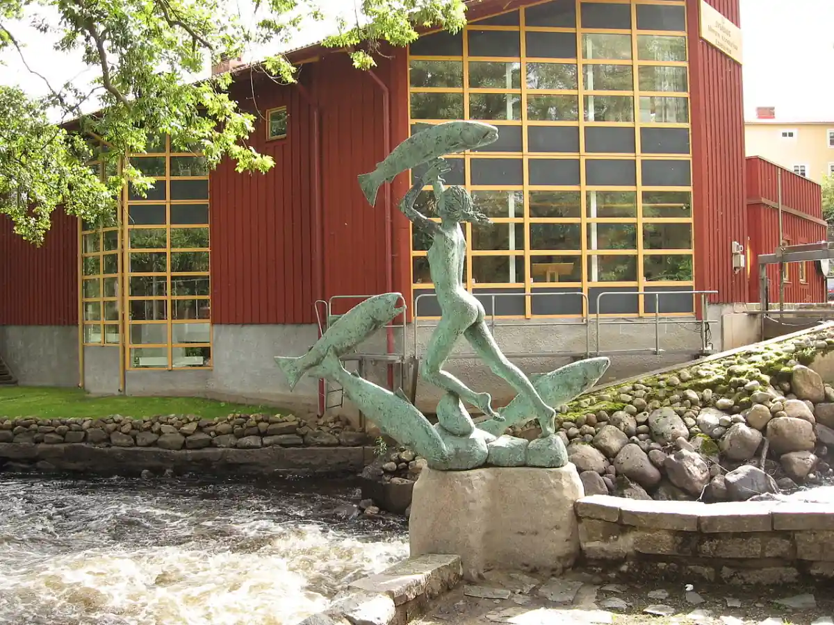 Skulptur i Mörrum vid fors och röd byggnad