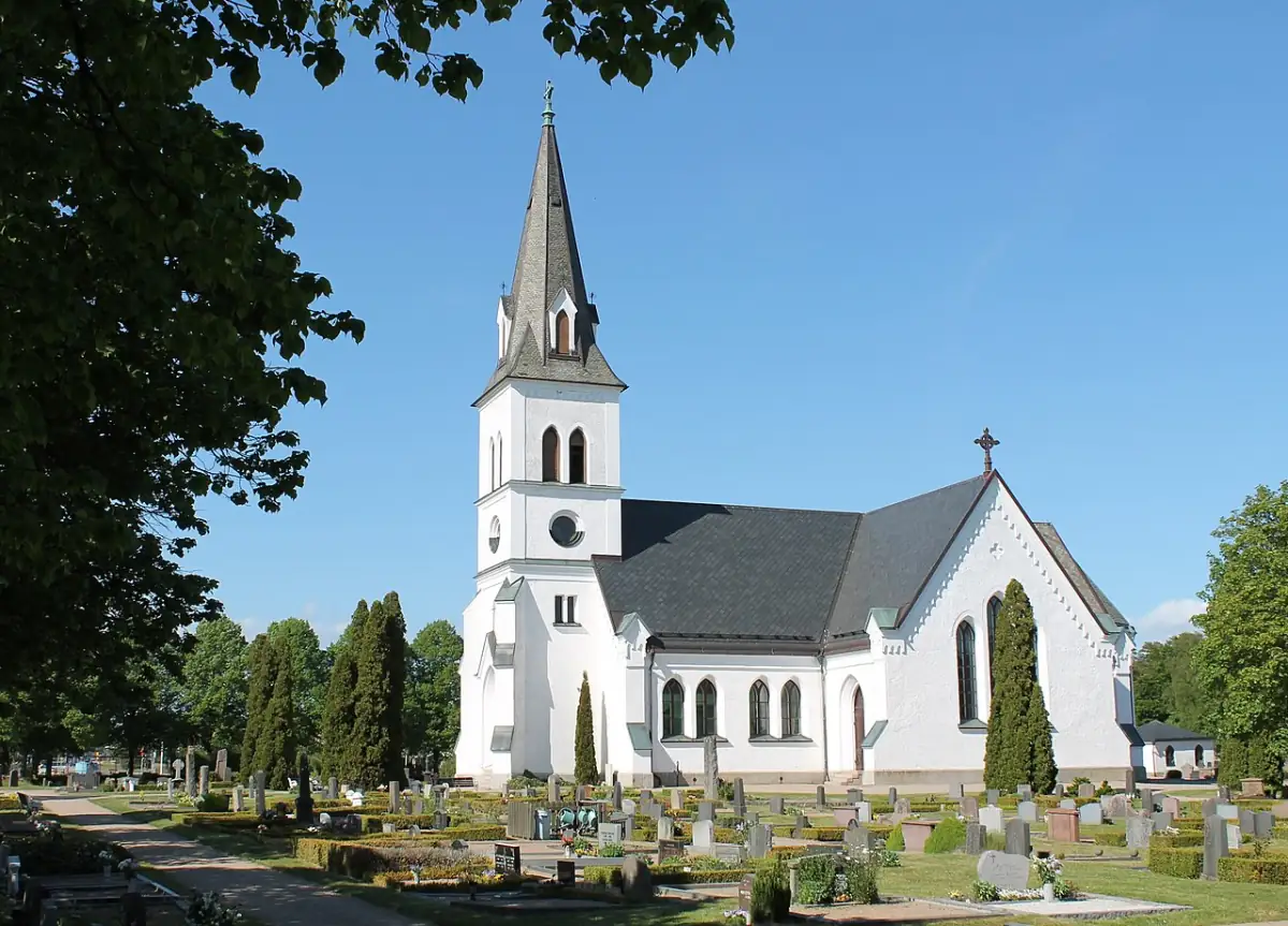 Vit kyrka i Rödeby med kyrkogård och träd