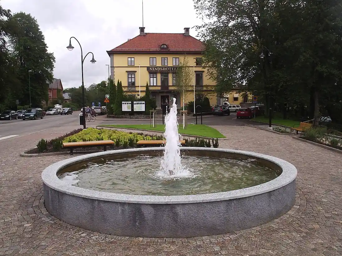 Fontän i Tidaholm med gul byggnad och gata