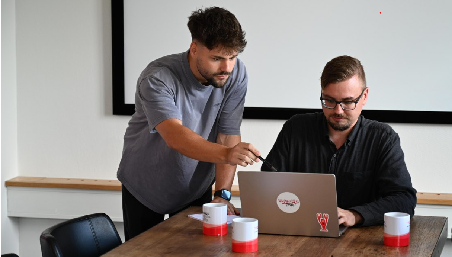 Zwei Männer schauen in einen Laptop und besprechen etwas.